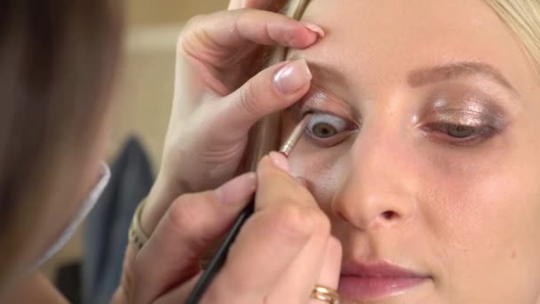 Hände eines professionellen Maskenbildners, der den Augen des Models Eyeliner aufträgt — Stockvideo