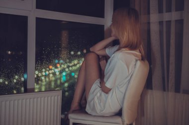 Beyaz gömlekli genç sarışın kadın çenesi yukarıda bir sandalyede oturur ve bir yerden bir tavana gece şehrini seyreder.