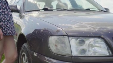 Bir kadın tarlada tek başına bir arabaya bakar. Araba çamura saplandı.,