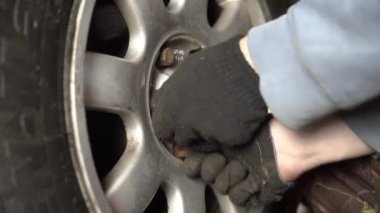 Otomobil tamircisi el anahtarıyla garajdaki bir arabanın tekerleğini söküyor..