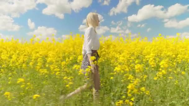 Женщина счастливо ходит по полю рапса и касается желтых цветов. — стоковое видео