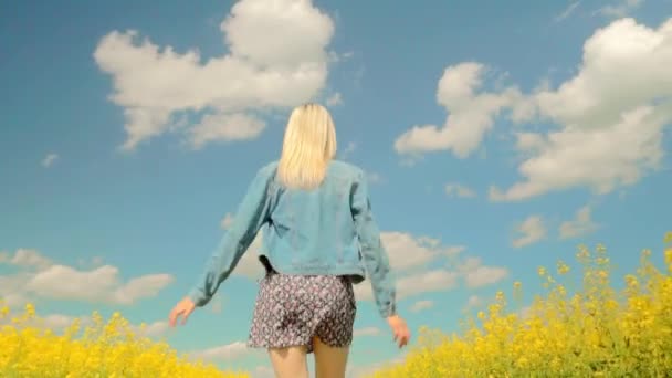 Kvinna springer snabbt genom ängen av blommande raps, leende, hennes armar öppna — Stockvideo