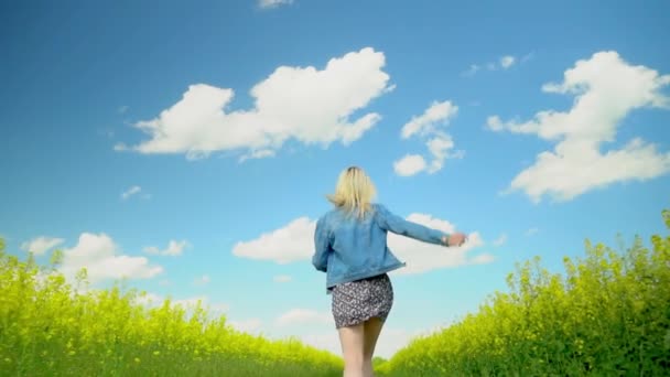Kobieta biegnie szybko przez łąkę kwitnącego rzepaku, uśmiechnięta, z otwartymi ramionami — Wideo stockowe
