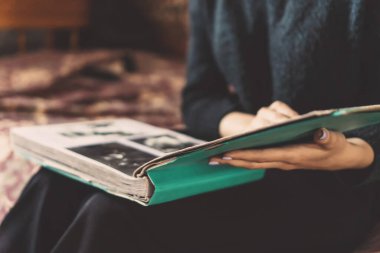 Koyu renk elbiseli bir kızın kucağında bir albüm tutarak eski fotoğraflara baktığı yakın plan.