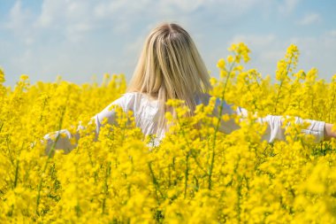 Beyaz tişörtlü genç sarışın kadın güneşli bir günde kollarını açarak kollarını kameraya uzatır.
