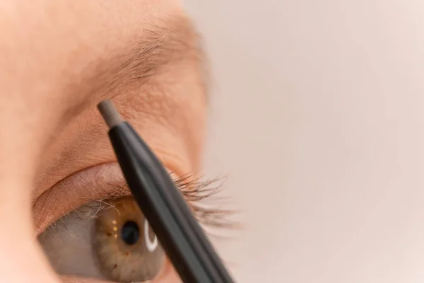 Makeup artist\'s hand draws eyebrows for a young girl with a pencil. Macrophotography. Selective Focus