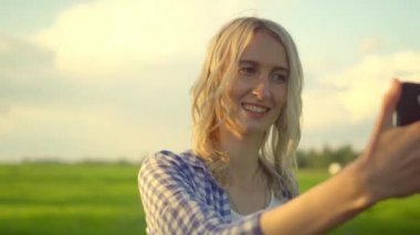 Güzel bir kadın yazın gün batımında akıllı telefonuyla selfie çeker..