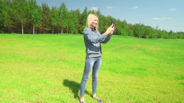 Portrét žena v džínách a bunda přičemž selfie v poli na venkově proti — Stock video