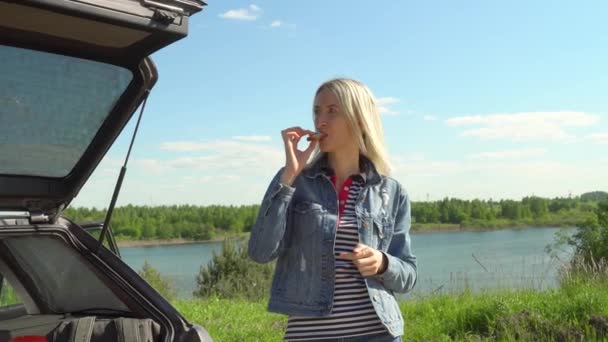 Genç ve güzel bir kadın arabasının yanında yemek yiyor. yol kenarında piknik. — Stok video
