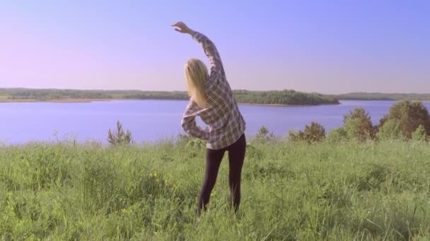 Una donna bella e sana fa esercizi in natura vicino all'acqua o uno stagno. — Video Stock