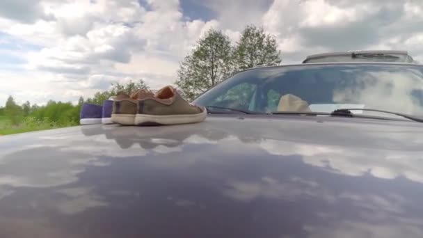 Две пары кроссовок стоят на капоте автомобиля и высушены или проветриваются. — стоковое видео