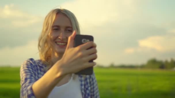 Een mooie vrouw neemt een selfie op haar smartphone in het veld in de zomer bij zonsondergang. — Stockvideo