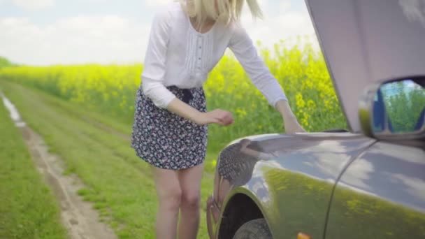 Mujer rubia joven en camisa y falda vierte líquido limpiaparabrisas en el coche — Vídeos de Stock