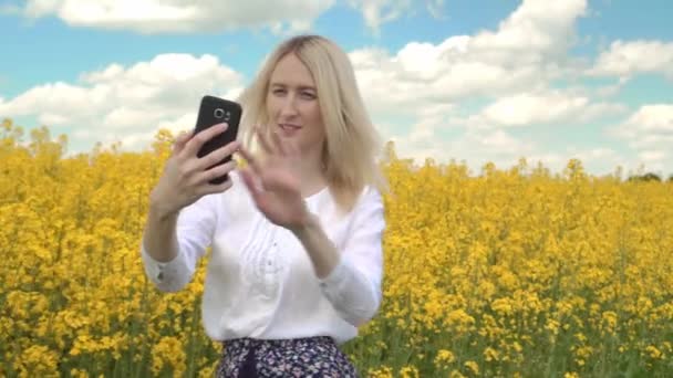 Retrato de una mujer feliz tomando selfie en un campo de flores de colza amarillas. — Vídeo de stock