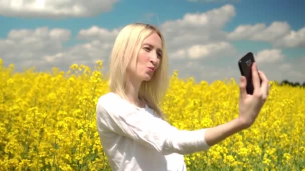 Retrato de uma mulher feliz tomando selfie em um campo de flores de colza amarelas. — Vídeo de Stock