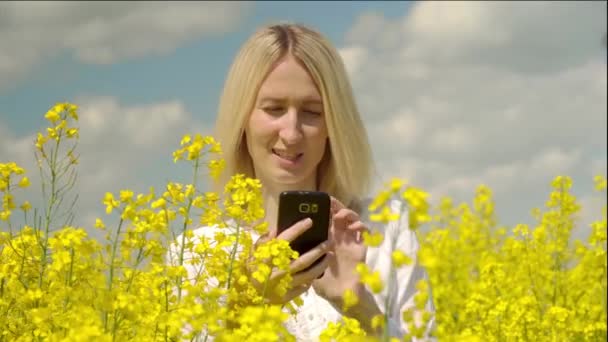 Ung vacker blond tar bilder av en blommande raps i ett fält — Stockvideo