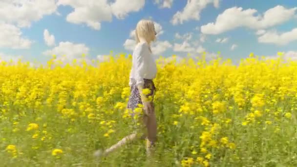 Kvinna går gladeligen genom ett fält av raps och vidrör gula blommor. — Stockvideo