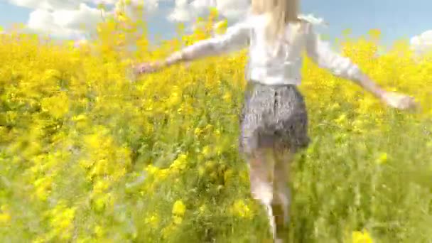 Mujer corre rápidamente a través del prado de colza floreciente, sonriendo, sus brazos abiertos — Vídeo de stock