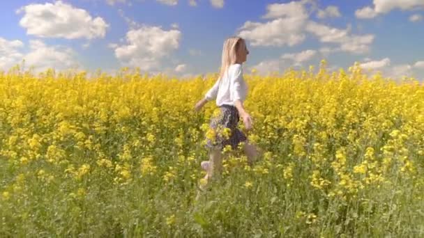 Mulher feliz caminha através de um campo de colza e toca flores amarelas. — Vídeo de Stock