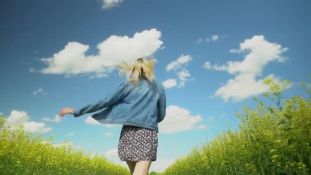 En ung kvinna springer genom ett fält av blommande raps. — Stockvideo