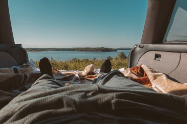 Durgun doğa gölü manzarası. Arabadan karavana orman. Güneşli bir yaz gününde ön planda insan ayakları var.