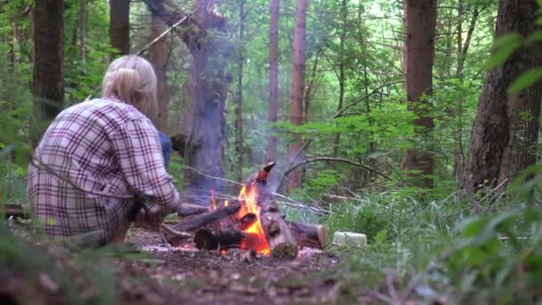Mladá krásná štíhlá žena, sedící u ohně a házející dříví do lesa. — Stock video