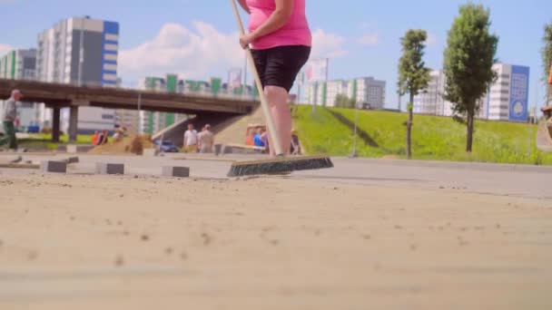 La main d'une femme balaie le sable sur la surface grise des dalles de béton avec un balai — Video