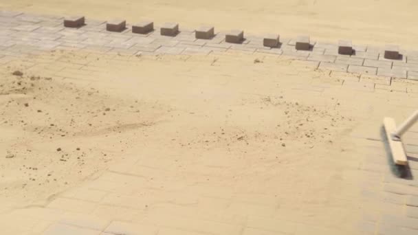 De hand van een vrouw veegt zand op het grijze oppervlak van betonnen platen met een bezem — Stockvideo