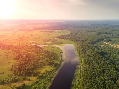 Güneşli bir akşamdan önce gölün, tarlaların, ağaçların güzel manzarasının drone görüntüsü.