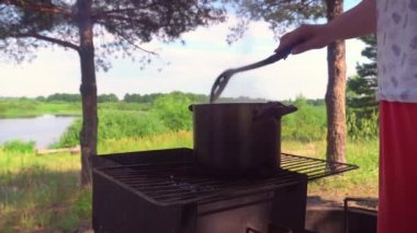 Kömürlü ızgara, tavada pişirme, bir kadın kaşıkla karıştırıyor..