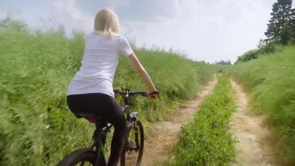 Dívka cestovatel jezdí na kole přes pole se zelenou trávou. Pomalu šlape.. — Stock video