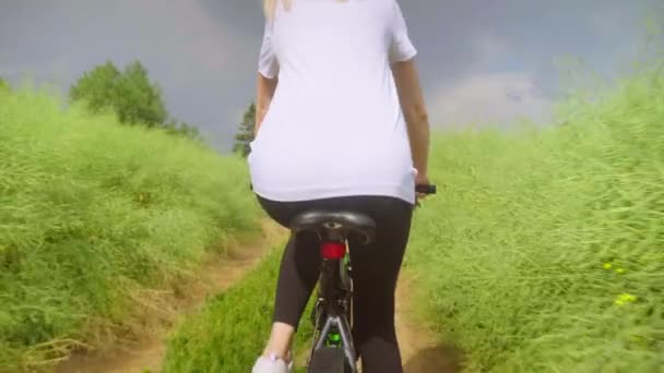 Uma menina monta uma bicicleta em uma estrada de campo no campo. Ela está feliz e sorrindo. — Vídeo de Stock