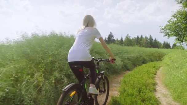 Meisje reiziger fietst door het veld met groen gras. Ze peddelt langzaam.. — Stockvideo