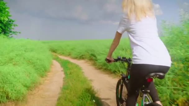 Menina viajante passeios de bicicleta através do campo com grama verde. Ela pedala devagar.. — Vídeo de Stock