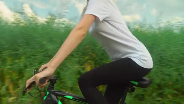 Uma menina monta uma bicicleta em uma estrada de campo no campo. Ela está feliz e sorrindo. — Vídeo de Stock