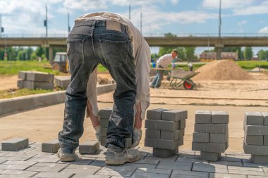 Çalışan adam yere bir sürü beton tuğla koyuyor. Döşeme döşemeleri