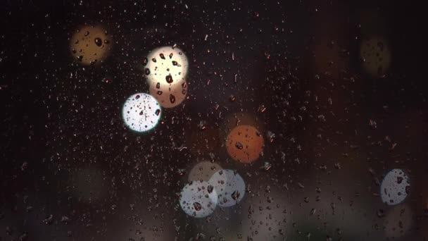 Bunte Lichter der Abendstadt und vorbeifahrende Autos durch ein nasses Regenfenster. — Stockvideo