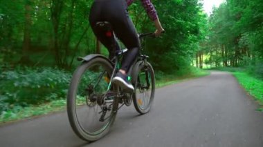 Ormanın ortasında asfalt bir yolda bisiklet sürüyor. Bacak ve tekerleklere yakın çekim.