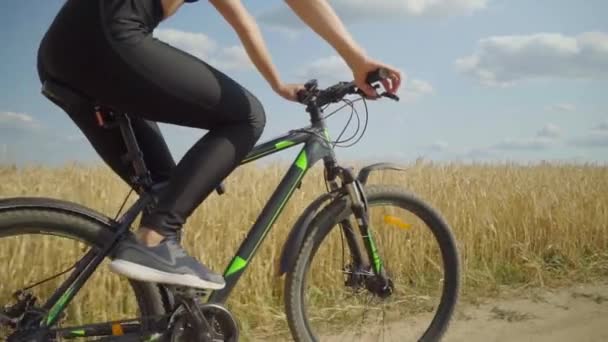 Une jeune femme fait du vélo sur une route rurale dans un champ par une journée ensoleillée. — Video