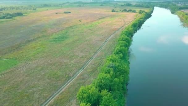 Een vogelperspectief van de drone. vrouw fietst in een veld langs de rivier — Stockvideo