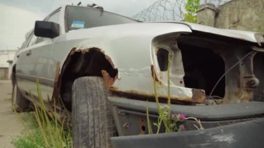 Otoparkta terk edilmiş paslı bir araba, çitlerle çevrili ve dikenli tellerle çevrili..