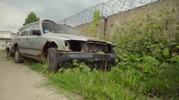 Zrezivělé opuštěné auto na parkovišti, obklopené plotem a ostnatým drátem. — Stock video