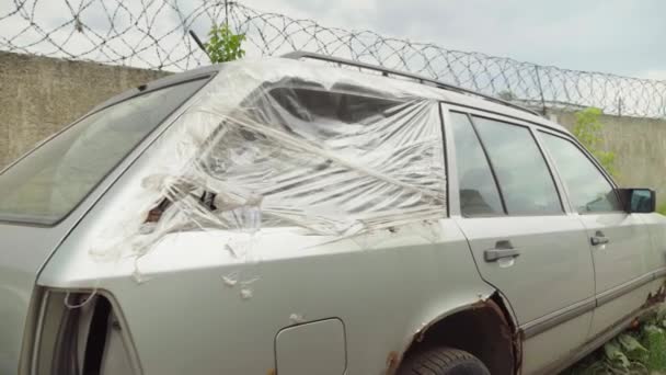 Una macchina arrugginita abbandonata nel parcheggio, circondata da recinzione e filo spinato. — Video Stock