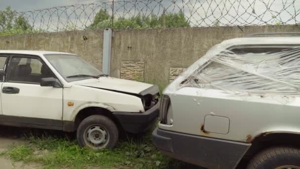 Um carro enferrujado abandonado no estacionamento, cercado por cerca e arame farpado. — Vídeo de Stock