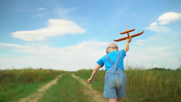 Happy boy runs with toy airplane across field in light of sunset. — Stock Video