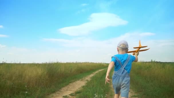 Anak laki-laki bahagia berjalan dengan mainan pesawat di lapangan dalam cahaya matahari terbenam. — Stok Video