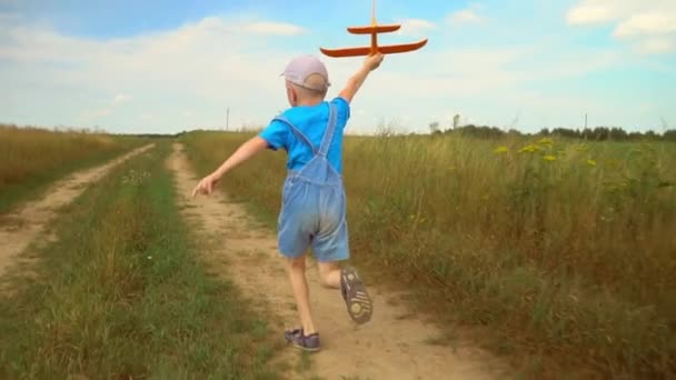 Gelukkig jongen loopt met speelgoed vliegtuig over veld in het licht van zonsondergang. — Stockvideo