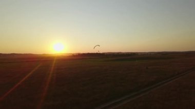 Paraşütün yeşil tarlalarında uçan bir paraşütçü silueti.