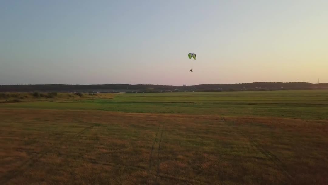 Paraşütün yeşil tarlalarında uçan bir paraşütçü silueti. — Stok video