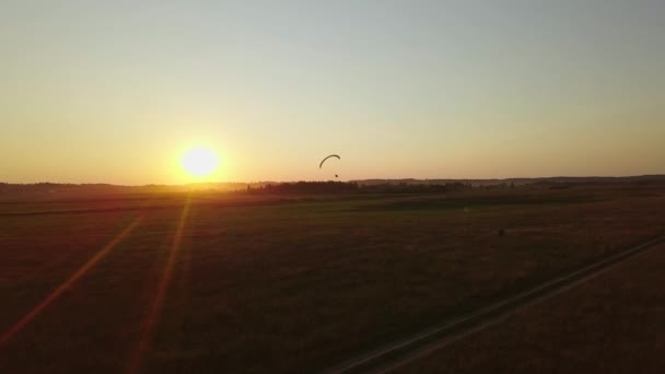 La silueta de un paramotor sobrevolando los verdes campos de un paracaídas — Vídeos de Stock